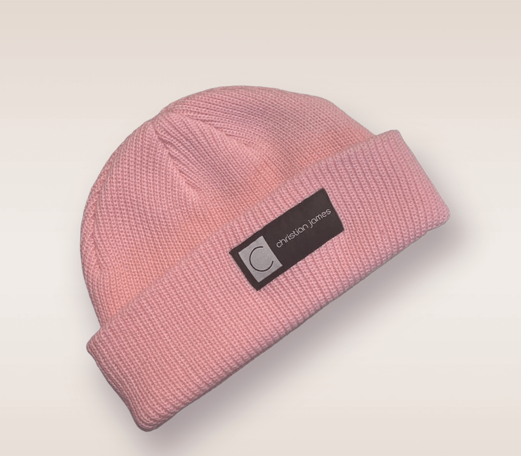 In this up-close shot, we are introduced to the Pink CJ beanie. A pink knit hat featuring an embroidered patch of the brand's acronym in black and white. 