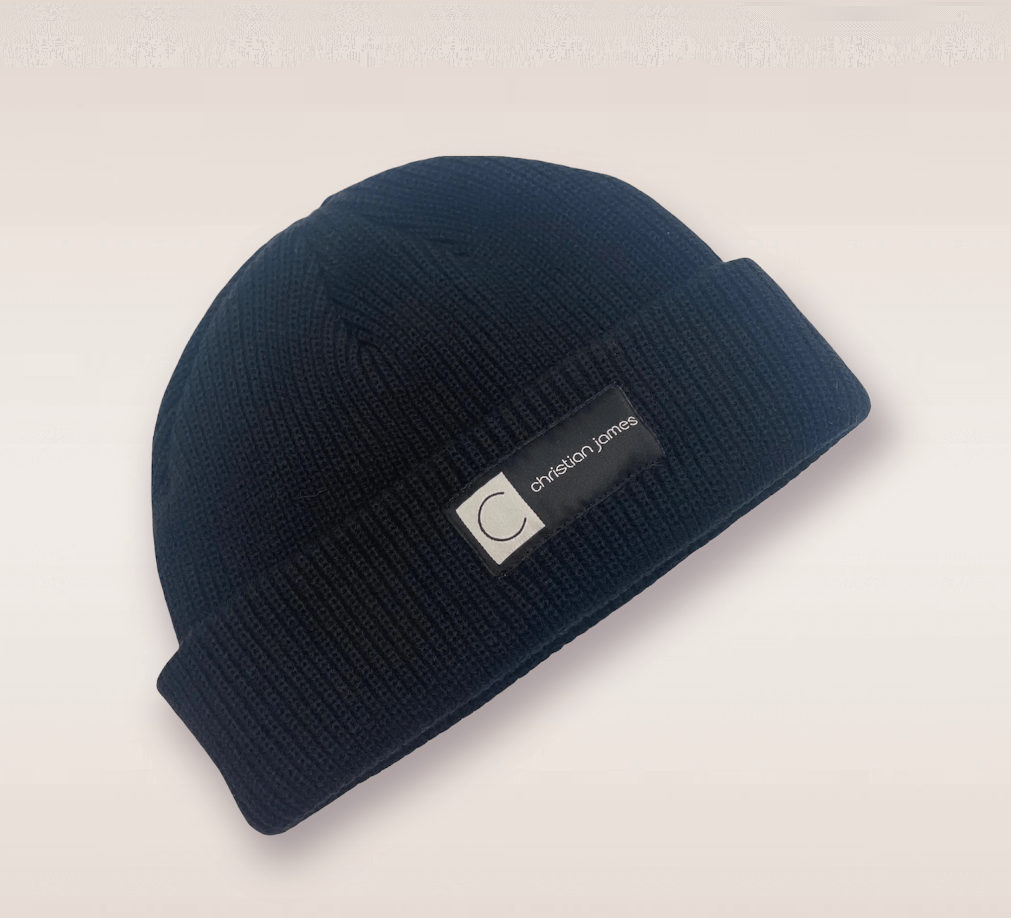 In this up-close shot, we are introduced to the Black CJ beanie. A black knit hat featuring an embroidered patch of the brand's acronym in black and white. 