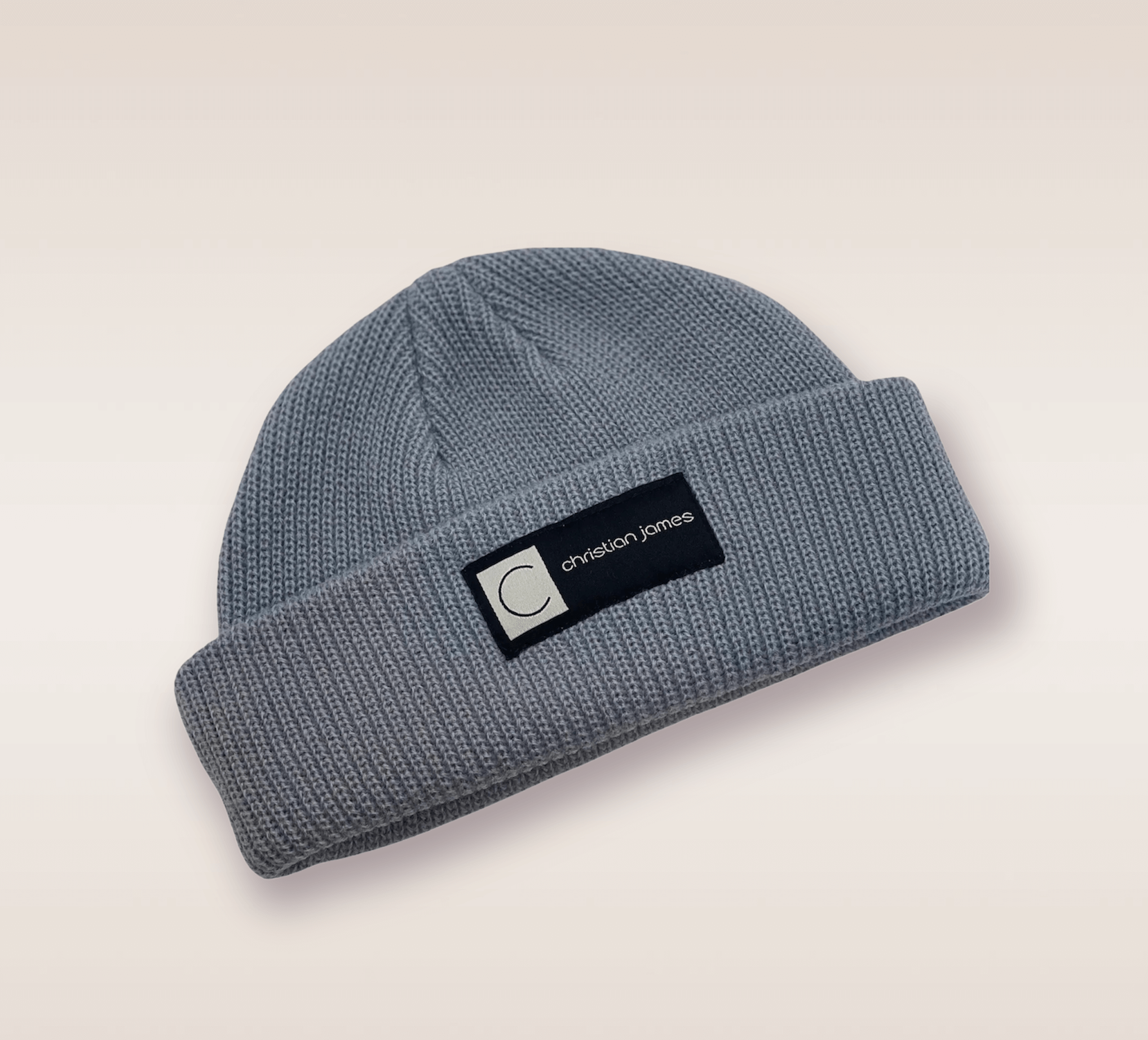 In this up-close shot, we are introduced to the Gray CJ beanie. A gray knit hat featuring an embroidered patch of the brand's acronym in black and white. 