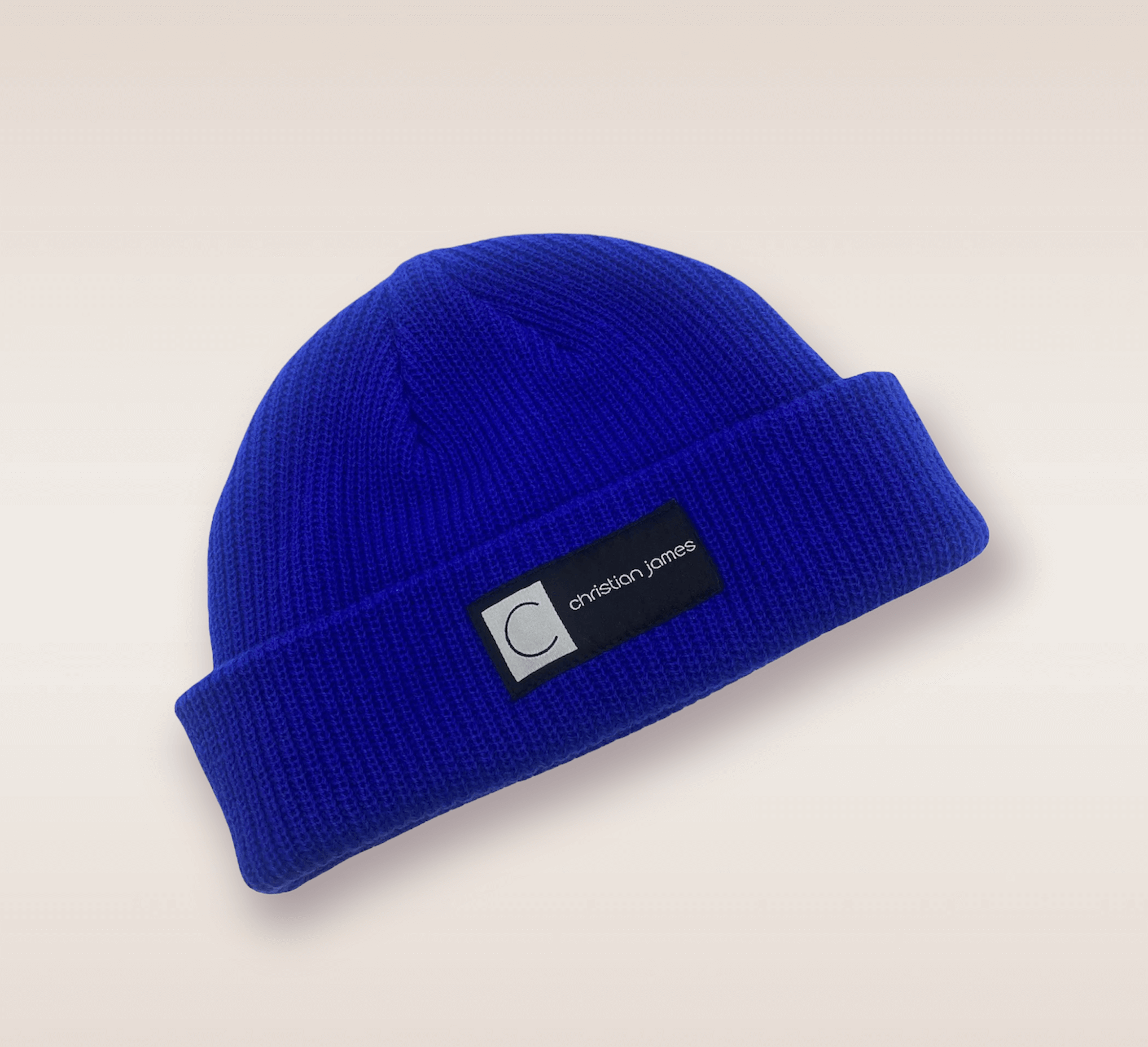 In this up-close shot, we are introduced to the Blue CJ beanie. A blue knit hat featuring an embroidered patch of the brand's acronym in black and white. 
