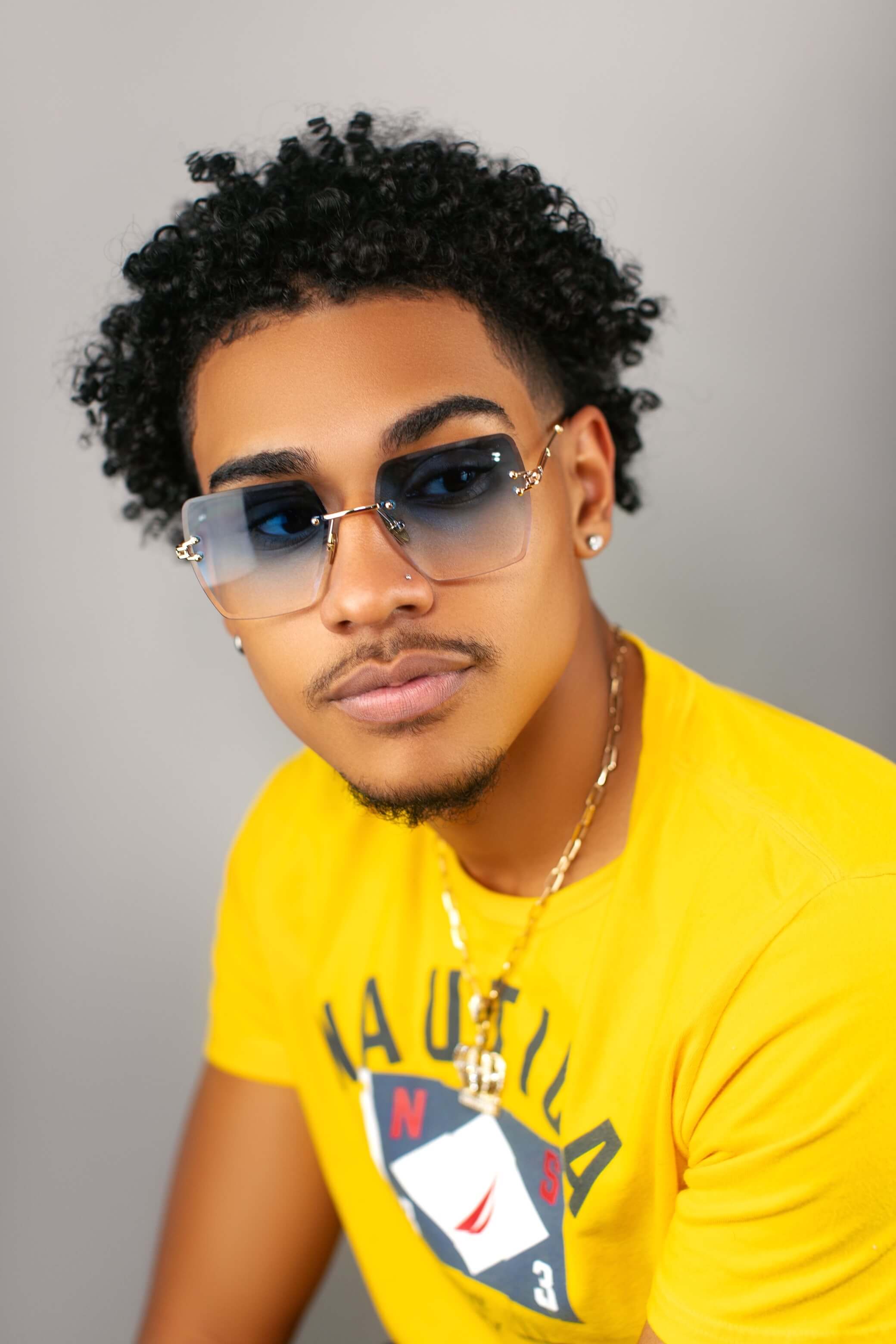 A man with a yellow shirt and gold chain, posing with a pair of Nipsey Blue Christian James frames