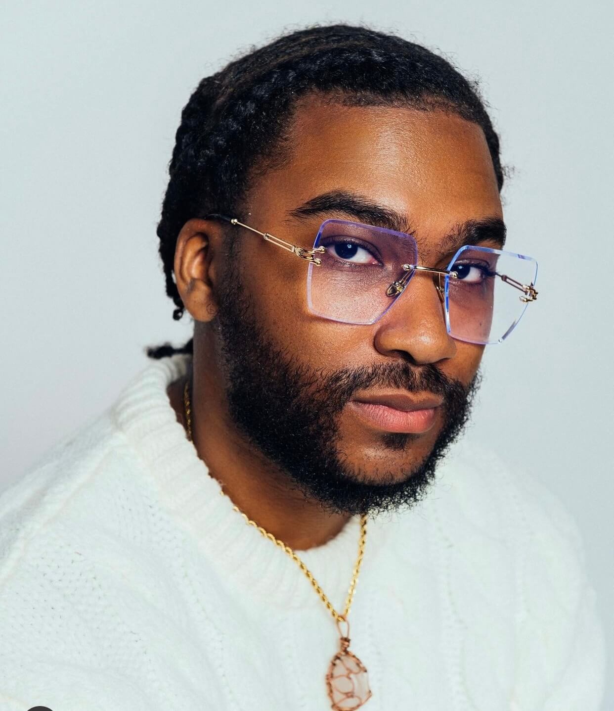 A man with a white ,fuzzy knit sweater, with a gold chain wearing the Nipsey Blue frames